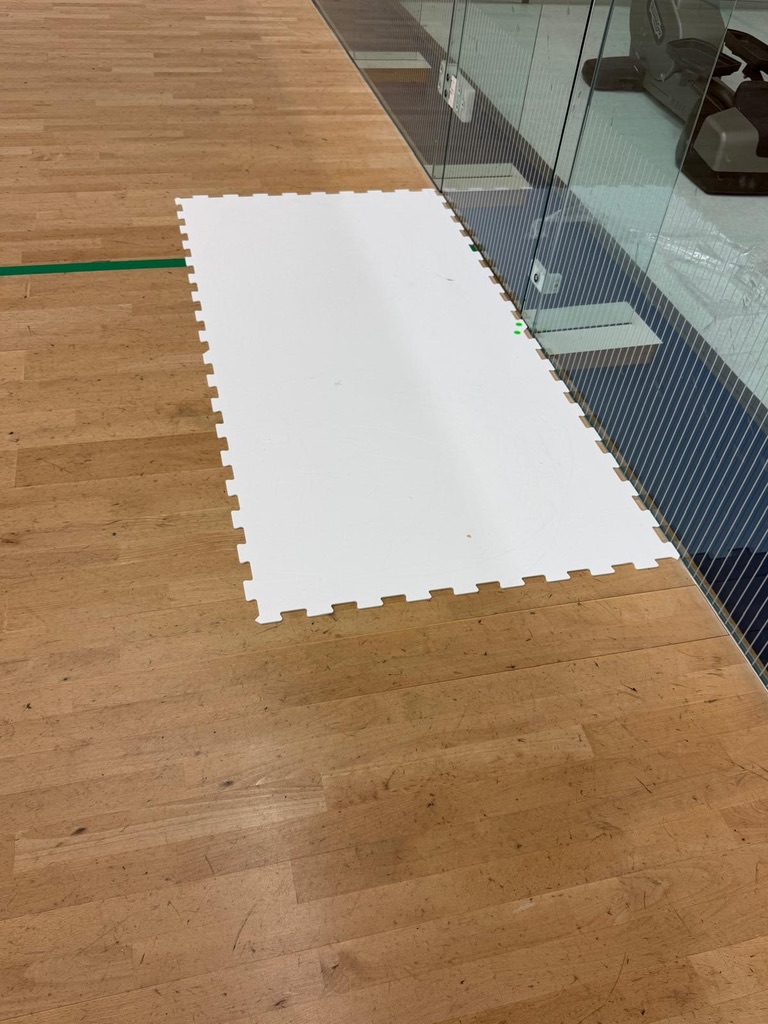 Weißes Green-Hockey-Bodenelement als Materialtest neben der Glaswand